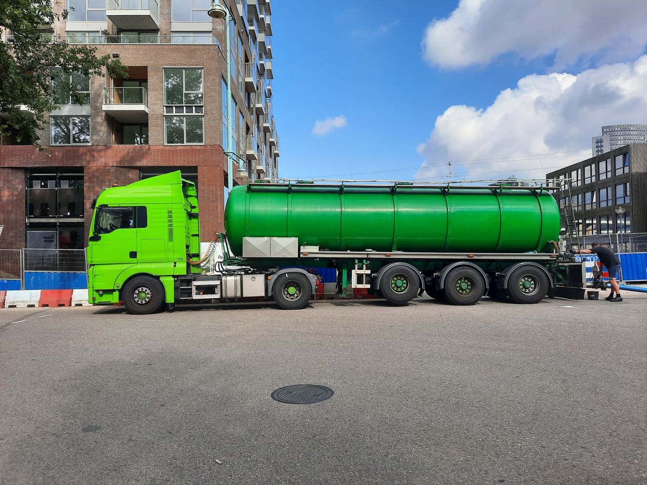 Green tanker truck parked in Amsterdam, urban street setting.